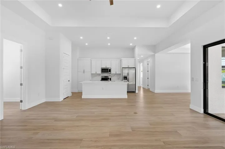 Kitchen with open floor plan, a kitchen island with sink, white cabinets, stainless steel appliances, and a raised ceiling