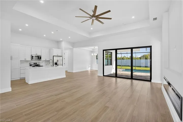 Unfurnished living room with ceiling fan, light wood finished floors, baseboard heating, a tray ceiling, and recessed lighting
