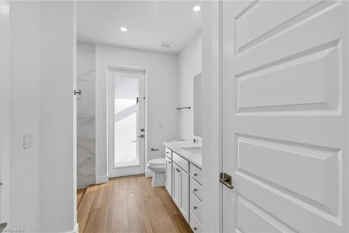 Full bath featuring vanity, light wood-style flooring, a marble finish shower, and recessed lighting