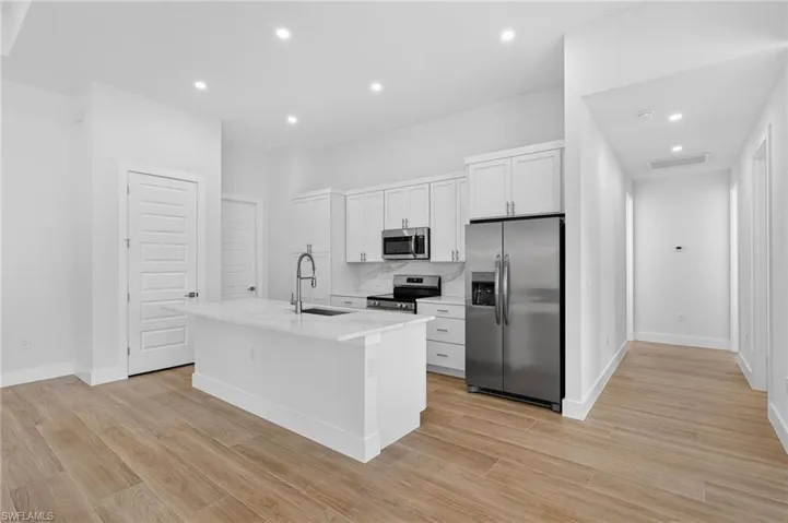 Kitchen with appliances with stainless steel finishes, white cabinetry, an island with sink, light stone counters, and recessed lighting