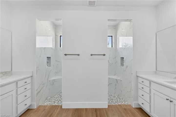 Full bath featuring two vanities, light wood-type flooring, and a marble finish shower