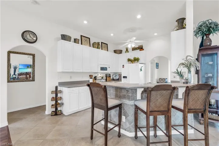 Kitchen featuring a breakfast bar area, white appliances, light tile patterned floors, white cabinets, and ceiling fan
