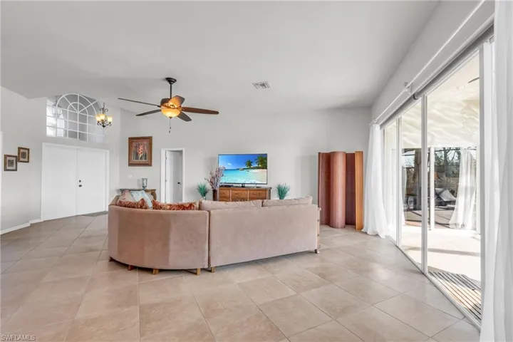 Living room with light tile patterned flooring and ceiling fan with notable chandelier