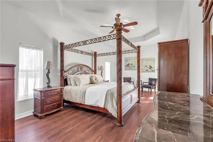 Bedroom with ceiling fan, dark hardwood / wood-style flooring, and a raised ceiling