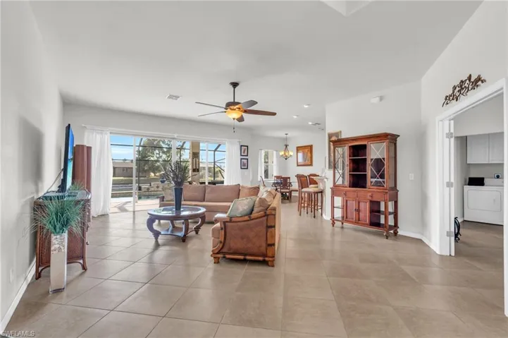 Living room with ceiling fan with notable chandelier, washer / clothes dryer, and light tile patterned floors
