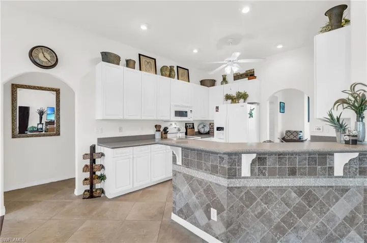 Kitchen featuring white appliances, a breakfast bar, light tile patterned floors, white cabinetry, and ceiling fan