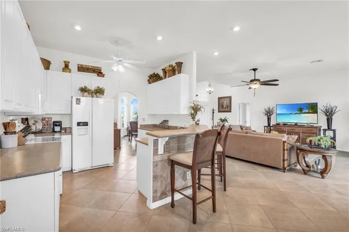 Kitchen featuring light tile patterned flooring, white cabinetry, a breakfast bar area, white fridge with ice dispenser, and ceiling fan
