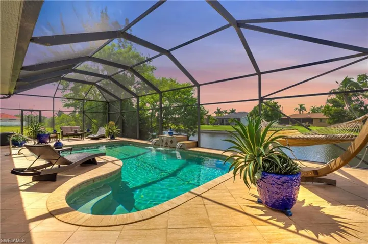 Pool at dusk with a jacuzzi, a patio, pool water feature, and a lanai