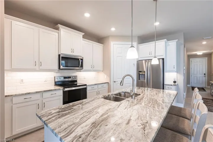 Kitchen with white cabinets, a kitchen breakfast bar, a sink, stainless steel appliances, and backsplash