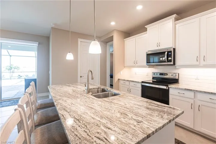 Kitchen with a center island with sink, appliances with stainless steel finishes, a sink, white cabinetry, and backsplash