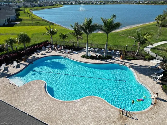 Community pool featuring a patio area, a water view, a lawn, and fence