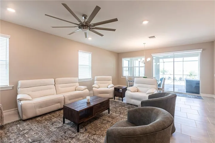 Living room with visible vents, baseboards, tile patterned flooring, ceiling fan with notable chandelier, and recessed lighting