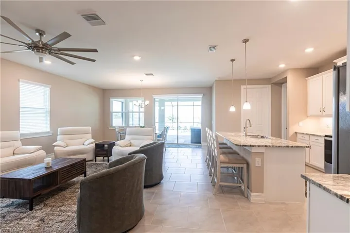 Living area with light tile patterned floors, ceiling fan with notable chandelier, visible vents, and recessed lighting