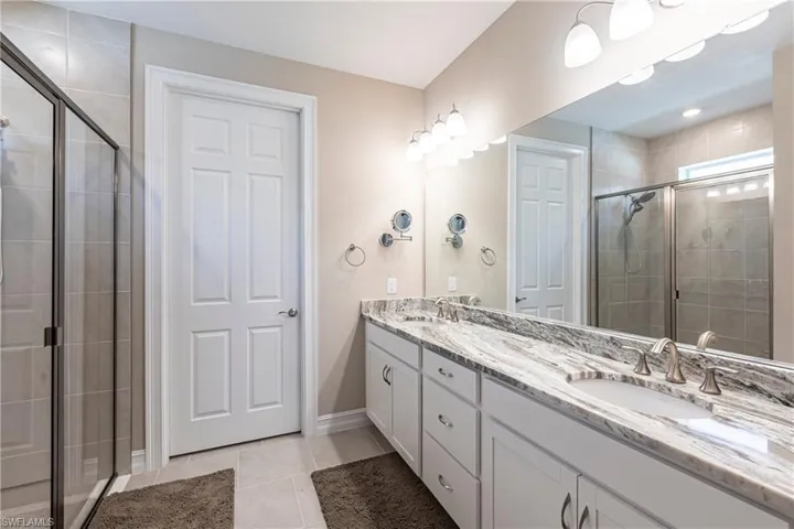 Bathroom with double vanity, a sink, a shower stall, and tile patterned floors