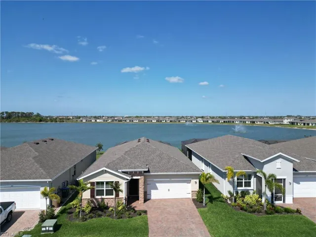 View of front of house featuring an attached garage, a water view, stone siding, decorative driveway, and a front yard