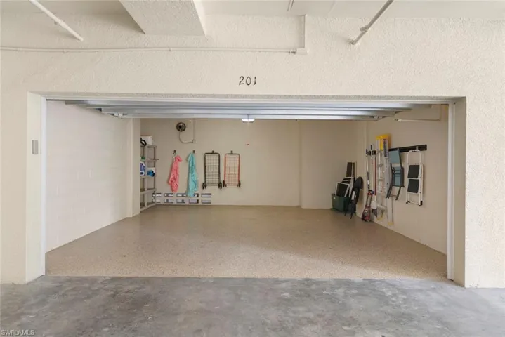 Enclosed garage stall featuring textured wall finishes, speckled epoxy flooring, and mounted wall storage racks