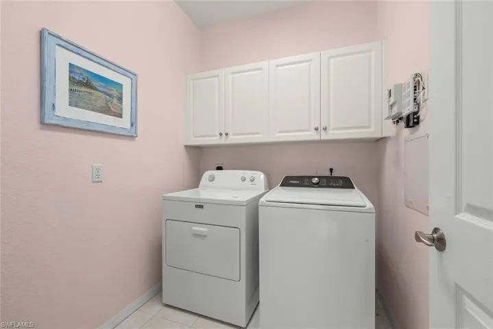 Laundry area featuring white shaker-style wall-mounted cabinetry, tile flooring, and a solid-core door with a brushed nickel lever handle