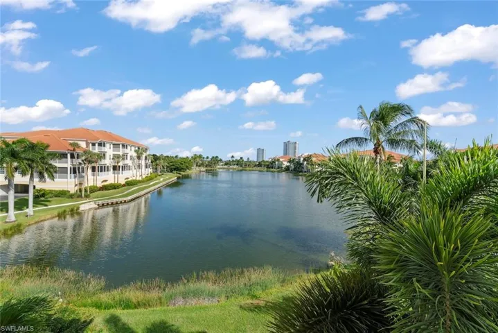 Waterfront property featuring a canal, mature palm trees, multi-story buildings with tile roofing, and manicured green space