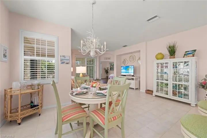 Dining area featuring tile flooring, a decorative chandelier, white plantation shutters, and a built-in display cabinet with glass doors