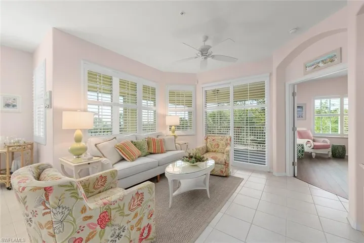 Living area featuring tile flooring, multiple windows with plantation shutters, a ceiling fan, and arched entryways