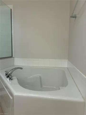 Corner soaking tub with chrome fixtures and surrounding white tile