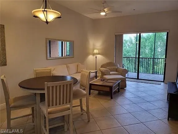 Open-concept living space with tile flooring, featuring a dining area with a round table, a ceiling fan, and sliding glass doors opening to a screened balcony