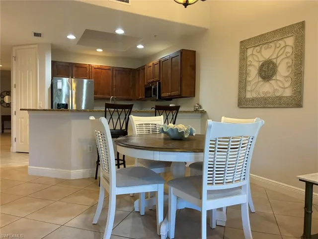 Integrated kitchen and dining area featuring tile flooring, recessed lighting, wood cabinetry, stainless steel appliances, and a breakfast bar