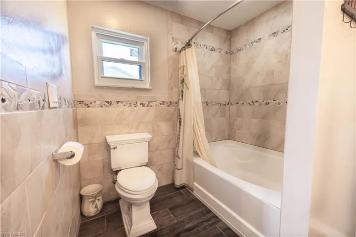 Bathroom with tile walls, toilet, and shower / tub combo with curtain