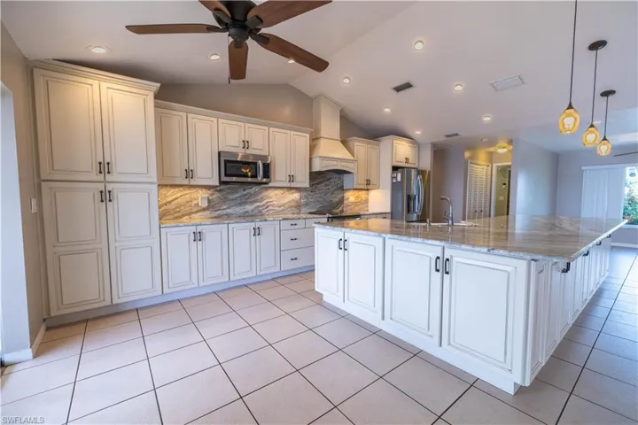 Kitchen featuring vaulted ceiling, appliances with stainless steel finishes, custom exhaust hood, a large island, and ceiling fan