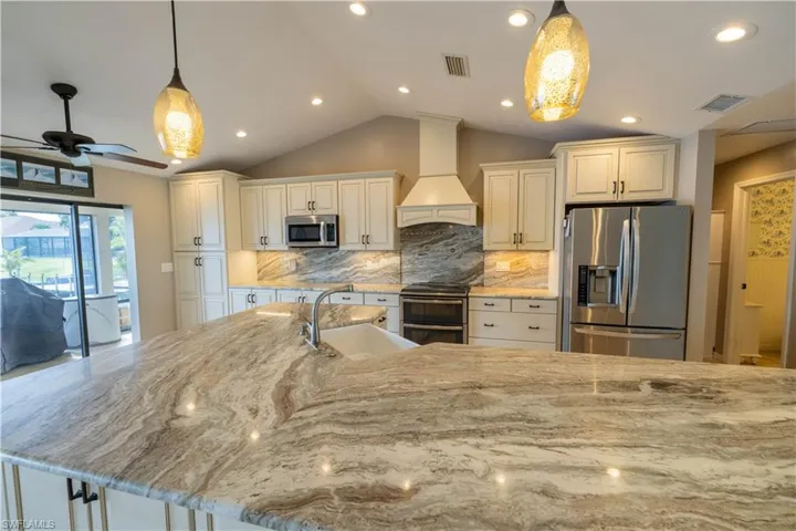 Kitchen featuring stainless steel appliances, premium range hood, sink, hanging light fixtures, and vaulted ceiling