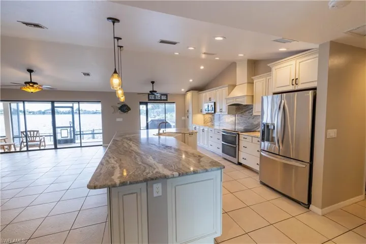 Dining area- vaulted ceiling, appliances with stainless steel finishes, a large island with sink, premium range hood, and ceiling fan