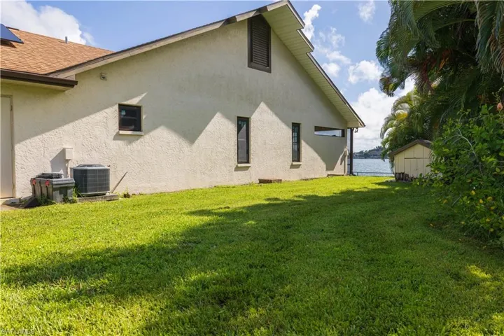 View of property exterior with cooling unit, a lawn, a shed, and a water view