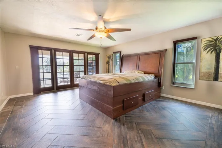Bedroom with multiple windows, ceiling fan, dark parquet floors, and french doors