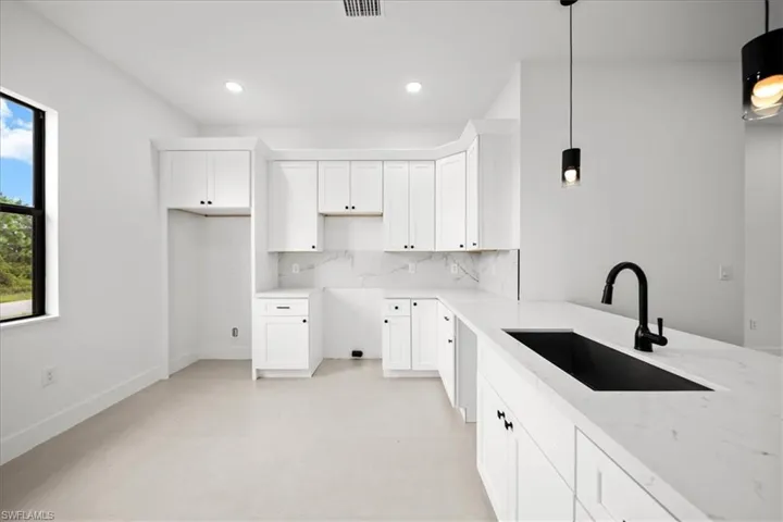 Kitchen with white cabinets, decorative backsplash, pendant lighting, light stone countertops, and recessed lighting
