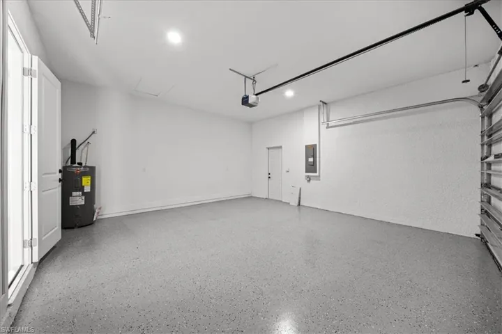 Garage featuring electric water heater, electric panel, a garage door opener, and recessed lighting