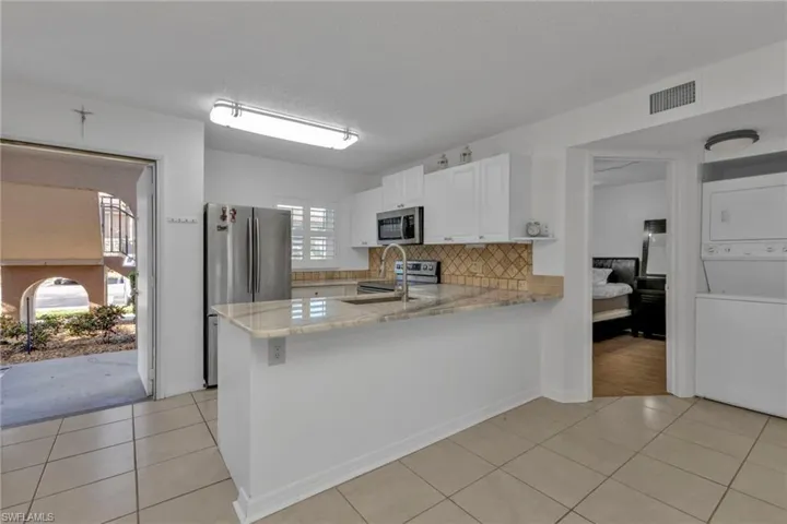Kitchen with appliances with stainless steel finishes, stacked washing machine and dryer, light tile patterned floors, backsplash, and a peninsula
