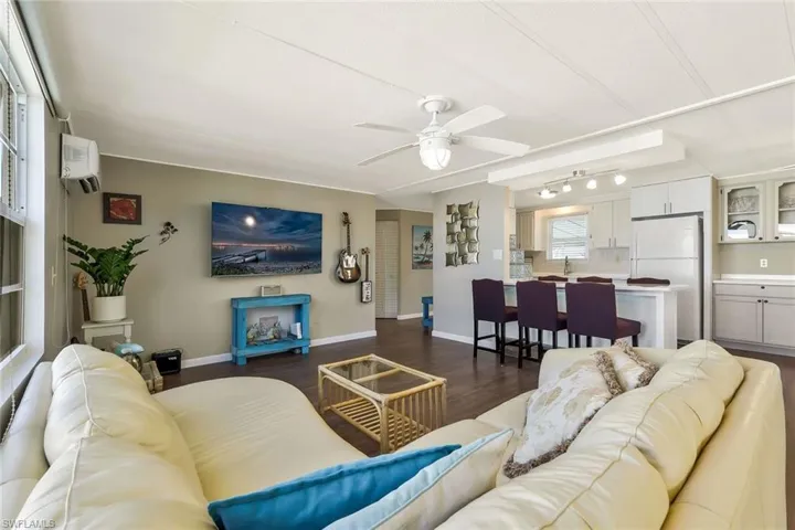 Living area with dark wood-style floors, a wall unit AC, ceiling fan, and baseboards