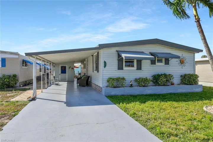 Manufactured / mobile home featuring a front yard, concrete driveway, and a carport
