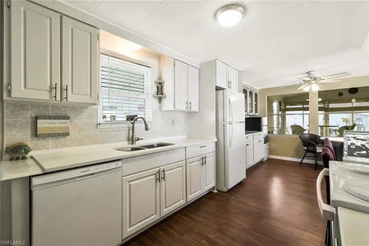 Kitchen featuring white appliances, dark wood-style flooring, backsplash, a sink, and a ceiling fan