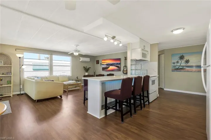 Kitchen with a wall unit AC, a breakfast bar, ceiling fan, and dark wood-type flooring