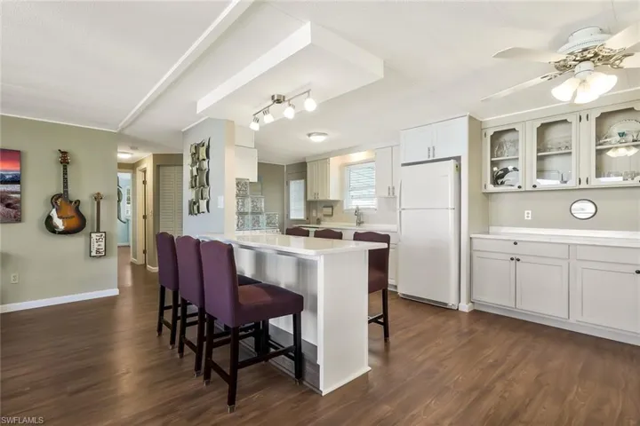 Kitchen featuring a kitchen bar, light countertops, dark wood-type flooring, freestanding refrigerator, and glass insert cabinets