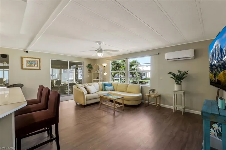 Living area featuring baseboards, a wall mounted AC, wood finished floors, and a ceiling fan