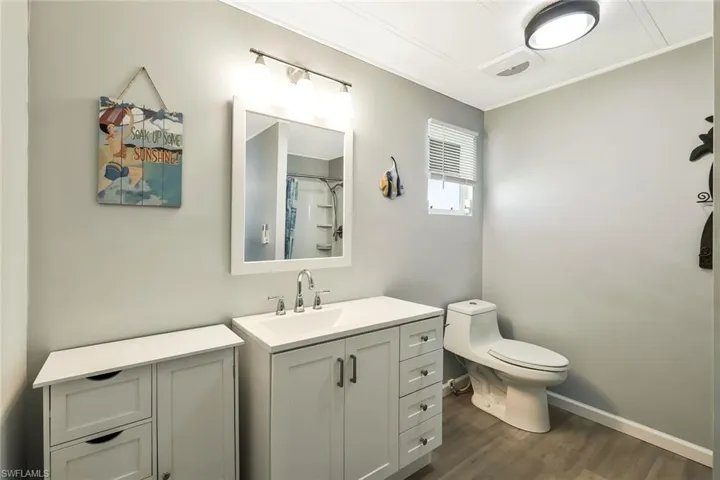 Full bath with toilet, vanity, baseboards, and wood finished floors
