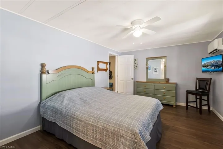 Bedroom with baseboards, wood finished floors, an AC wall unit, and a ceiling fan