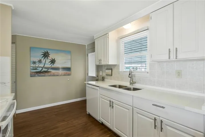 Kitchen featuring decorative backsplash, white cabinets, a sink, dark wood-style floors, and white dishwasher