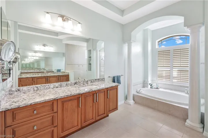 Bathroom featuring tile patterned flooring, tiled bath, vanity, and ornate columns