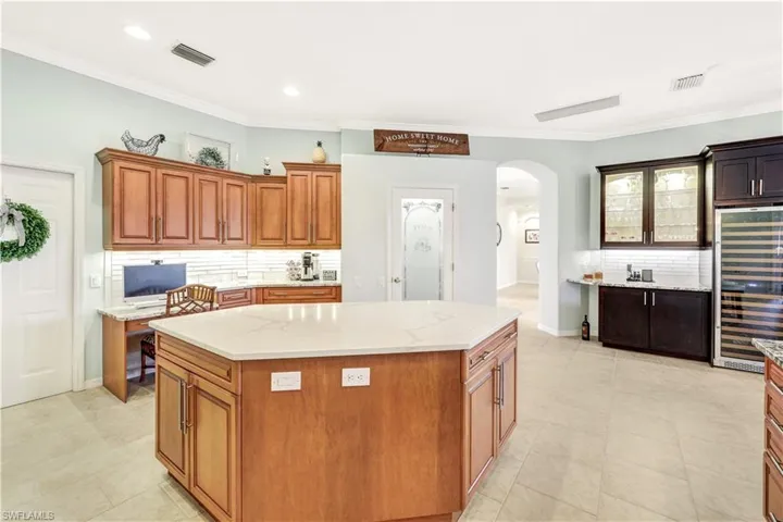 Kitchen featuring a kitchen island, wine cooler, light tile patterned floors, and backsplash