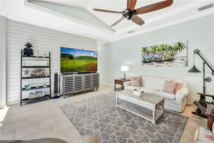 Living room with a tray ceiling, light tile patterned floors, crown molding, and ceiling fan