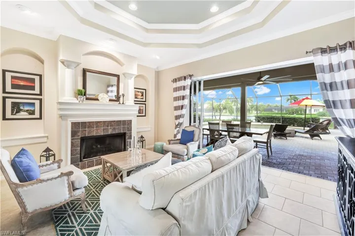 Living room featuring a raised ceiling, a tile fireplace, crown molding, ceiling fan, and light tile patterned flooring