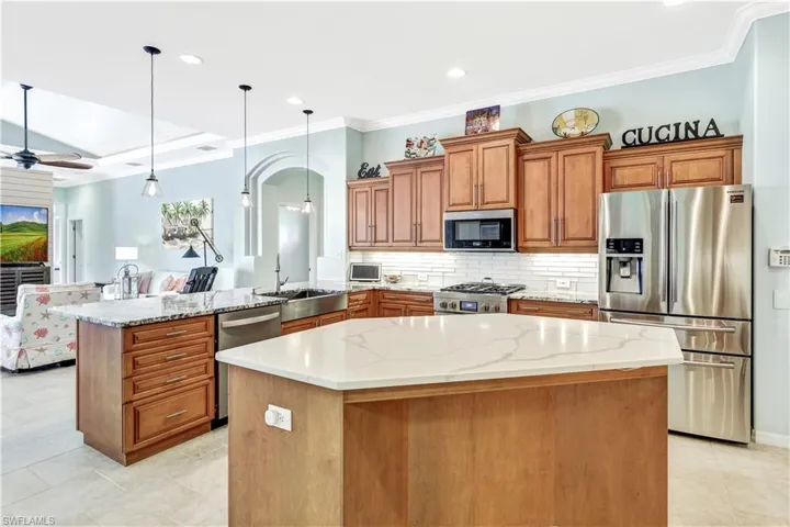 Kitchen with decorative light fixtures, light stone counters, stainless steel appliances, and a kitchen island